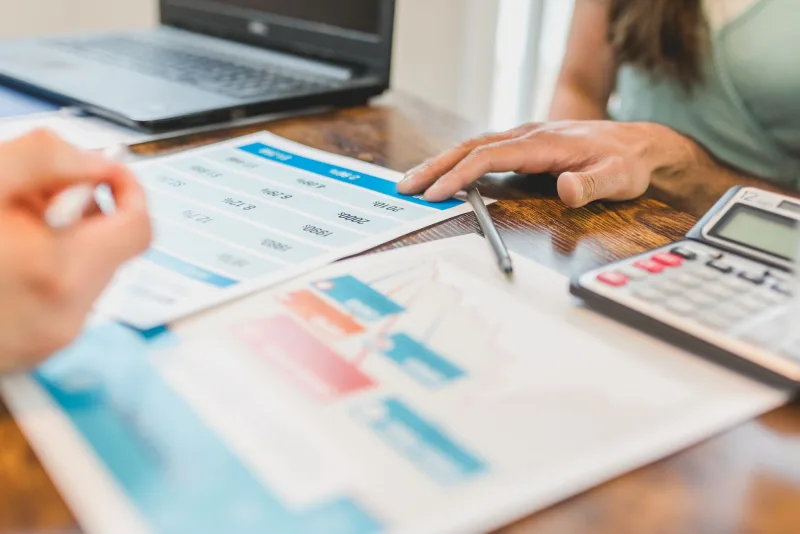 A close-up of hands examining business reports and a calculator.